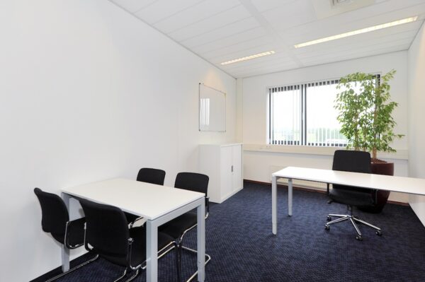 Modern ingerichte kantoorruimte aan de Laan van S-Gravenmade met wit meubilair, zwarte stoelen en een grote kamerplant bij het raam.